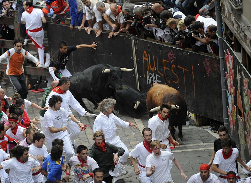 Corredores y toros derrapan en una curva durante el encierro.