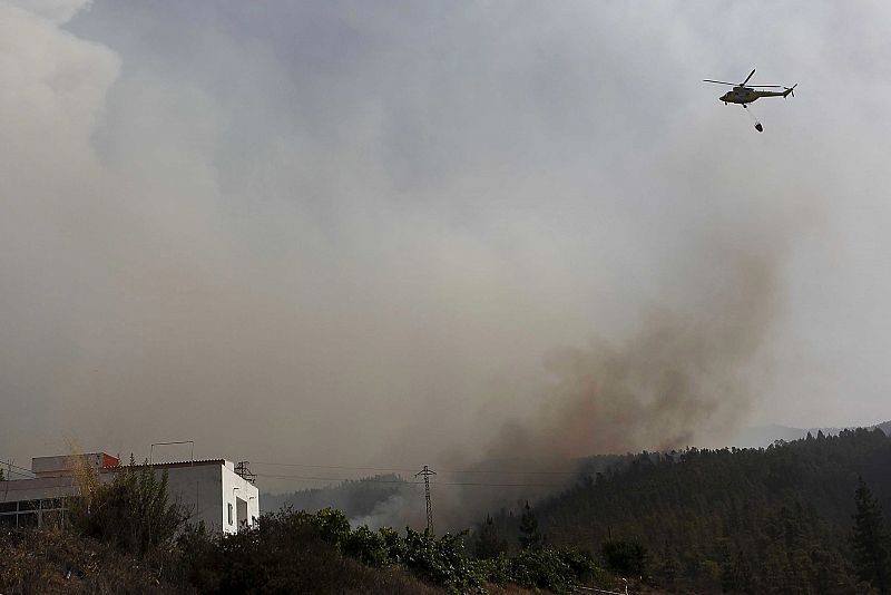 Uno de los siete helicópteros trabajan en la extinción del incendio forestal declarado ayer tarde en el sur de la isla de Tenerife que ha arrasado en las últimas horas unas 1.200 hectáreas y avanza en dos frentes, obligando a desalojar cuatro núcleos