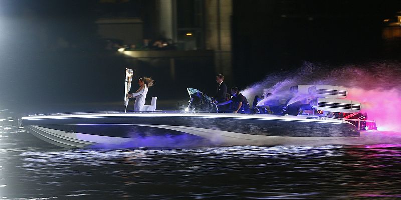 Britain's David Beckham drives a powerboat with the Olympic torch as fireworks are launched over Tower Bridge during the opening ceremony of the London 2012 Olympic Games