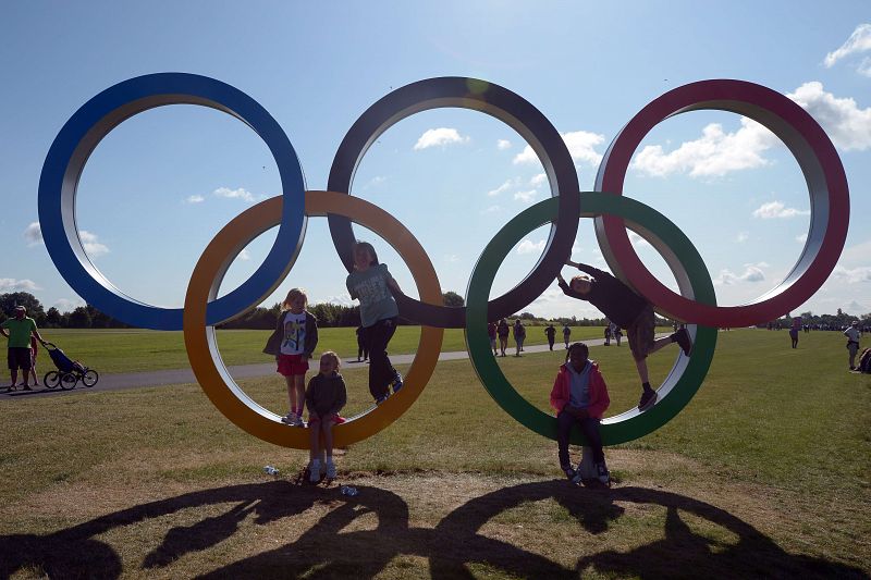 Niños jugando alrededor a los aros olímpicos.