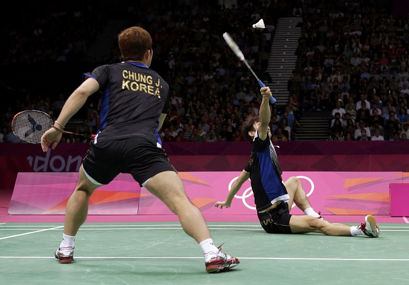South Korea's Lee Yong-dae returns a shot while sitting on the court as his teammate Chung Jae-sung looks on during their men's doubles badminton semifinal match against Denmark at the London 2012 Olympic Games at the Wembley Arena