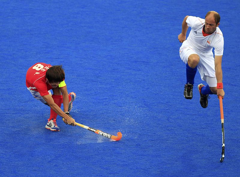 Teun de Nooijer de el equipo holandés (R) salta para evitar la pelota del jugador Lee Seungil de Corea del Sur durante el partido de hockey masculino del Grupo B.