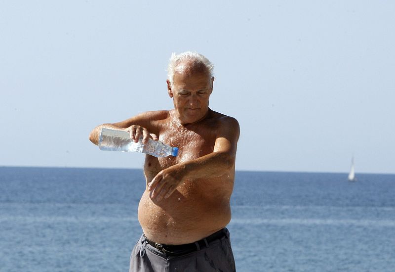 Un hombre se refresa el cuerpo en la playa de la Barceloneta con una botella de agua