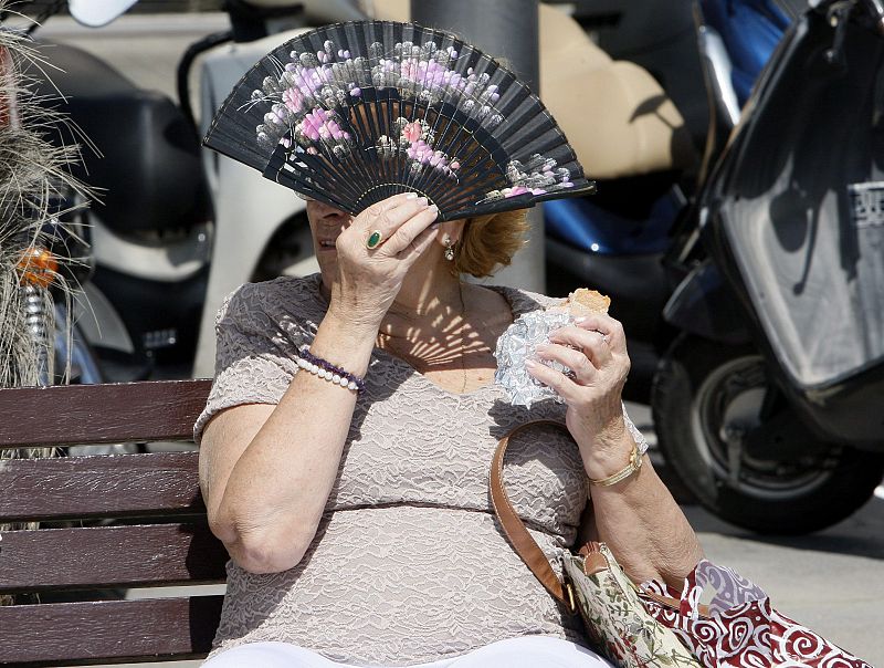 Una mujer se cubre la cara con un abanico en el barrio maritimo de la Barceloneta para protegerse del calor