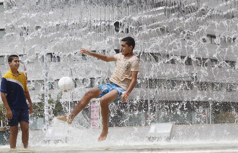 Unos jovenes juegan con una pelota en una de las fuentes del centro de Cordoba, donde se esperan altas temperaturas