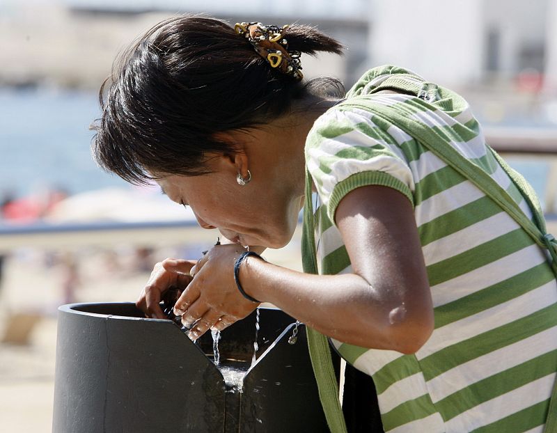 Una mujer se refresca en una fuente de Barcelona