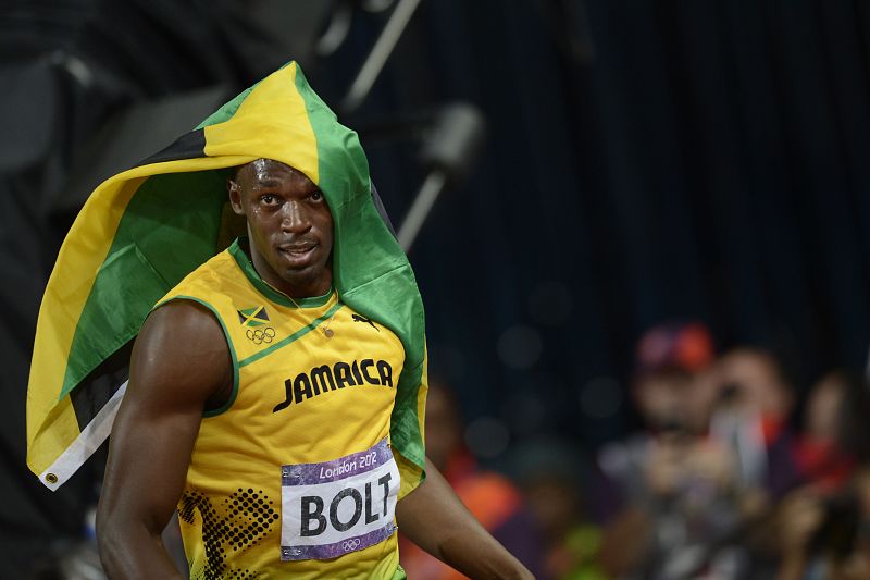 Bolt celebra su victoria enfundado en la bandera de Jamaica.