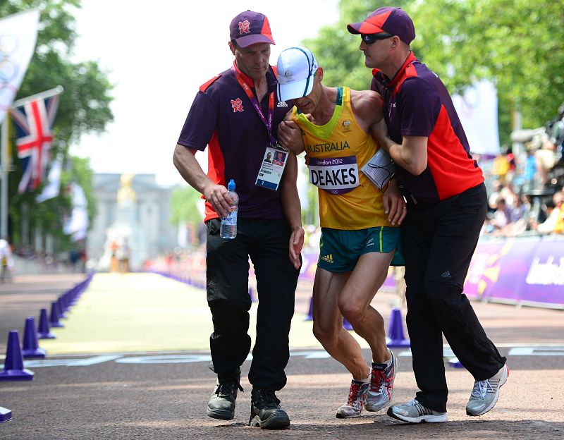 El marchador australiano Nathan Deakes (C) ayudado por voluntarios tras cruzar la línea de meta de los 50 km marcha.