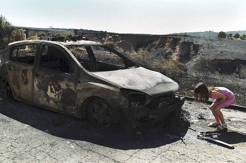 Una niña observa un coche d ela Guardia Civil abrasado en un incendio en Guadalajara