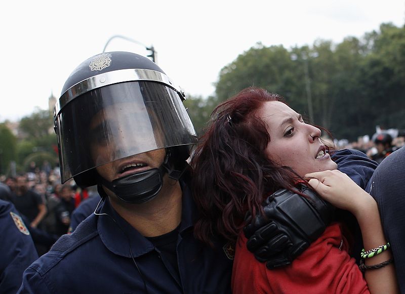 Protester grimaces as she is dragged away by riot police outside Spanish parliament in Madrid
