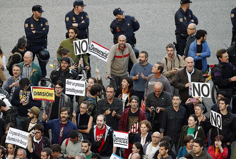 Protesters hold banners and shout slogans as Spanish National Police officers stand guard during a demonstration outside Madrid's Parliament
