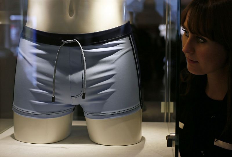 A employee poses next to a pair of swimming trunks, worn by Daniel Craig in the film "Casino Royal", during a media preview of "50 Years of James Bond - the Auction", at Christie's in London