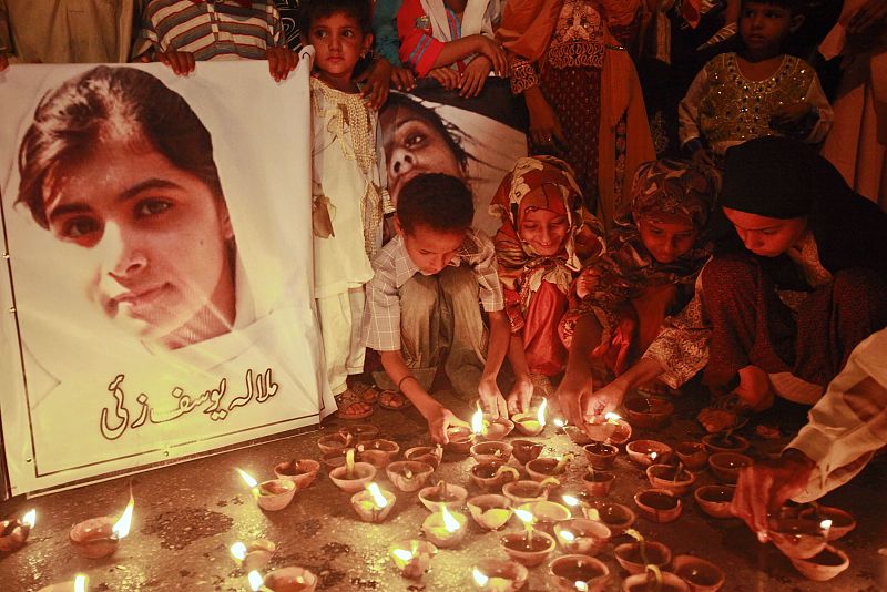 Children light oil lamps beside a picture of Malala Yousufzai at a school in Peshawar