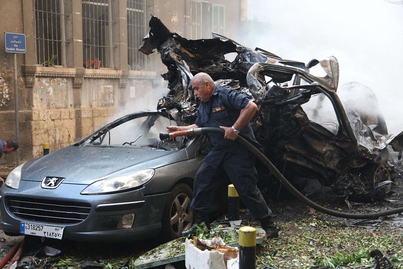 Un bombero libanés extingue el fuego de los vehículos incendiados en el lugar del atentado.