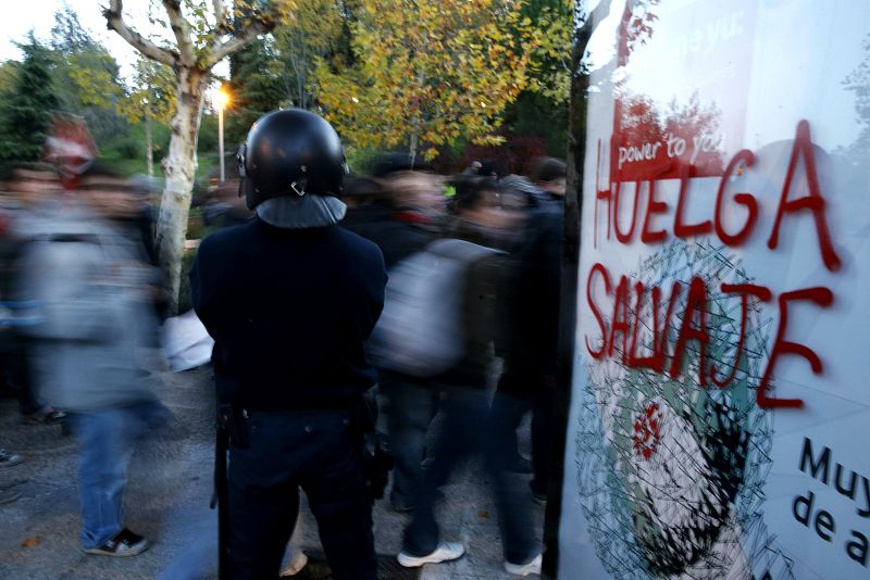 Un agente de Policía vigila en la Ciudad Universitaria de Madrid junto a una pintada relativa a la huelga general