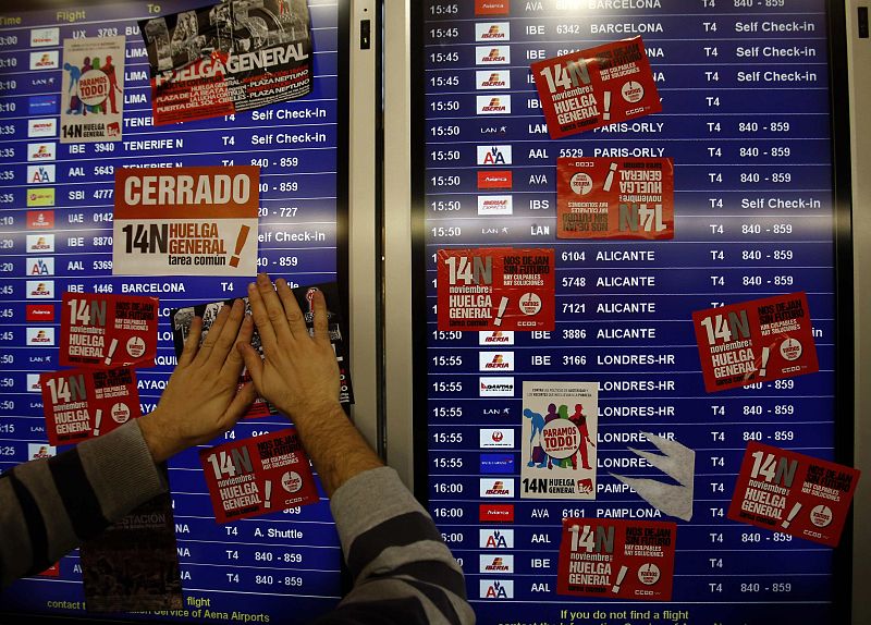 Unos piquetes informativos estampan pegatinas en las pantallas de información de la T4 del aeropuerto de Barajas de Madrid