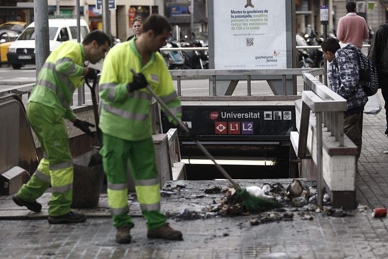 Operarios de limpieza retiran restos de un pequeño incendio en las puertas de una estación de metro de Barcelona