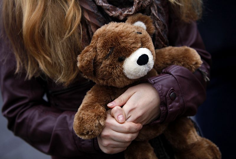 Woman carries a teddy bear to a makeshift memorial in Newtown, Connecticut