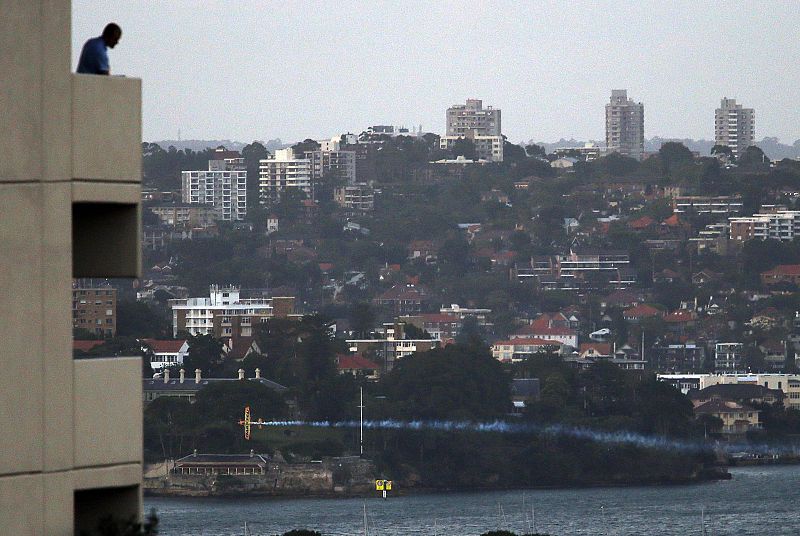Man watches from his balcony as a stunt plane flies low over Sydney Harbour, during a show prior to New Year's celebrations