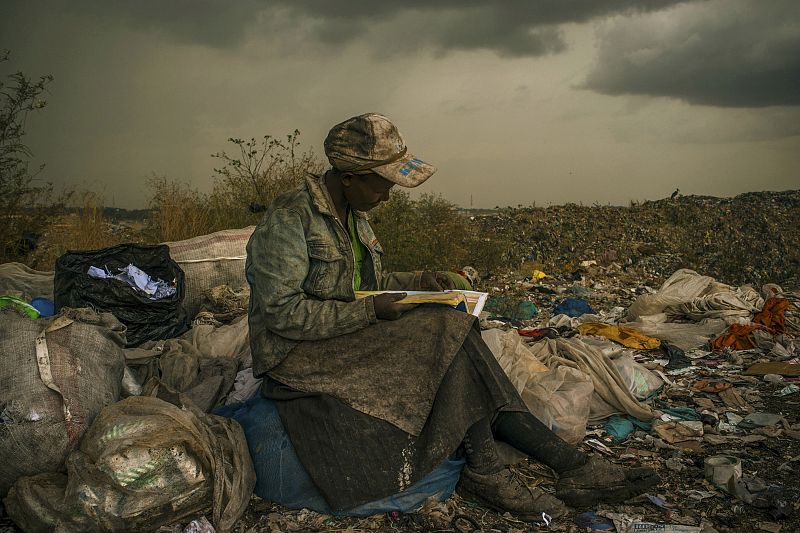 Imagen que ha ganado el primer premio en la categoría Temas Contemporáneos del World Press Photo en la que se ve una mujer, que trabaja rebuscando entre la basura, tomándose un descanso bajo la lluvia y ojeando un libro