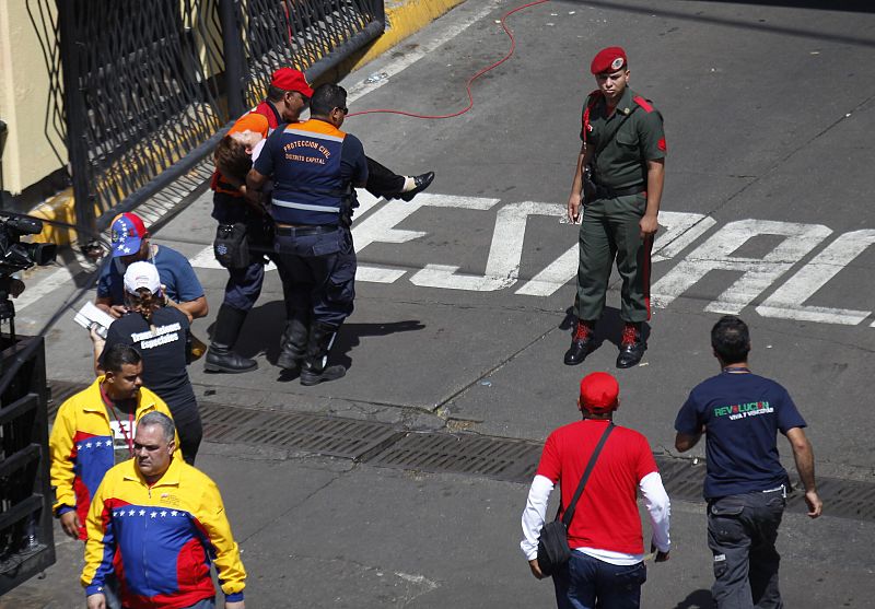 Dos miembros de Protección Civil venezolana llevan a una mujer que se ha desmayado cuando acompañaba al féretro del fallecido presidente de Venezuela, Huco Chávez