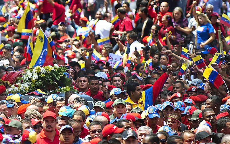 El vicepresidente venezolano Nicolás Maduro, en el centro de la imagen, alza el puño en medio de la 'marea roja' que ha acompaña al féretro de Chávez por las calles de Caracas