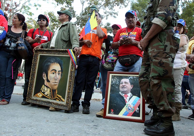 Un grupo de chavistas observan la carroza fúnebre con un retrato de Chávez junto a otro de Simón Bolívar