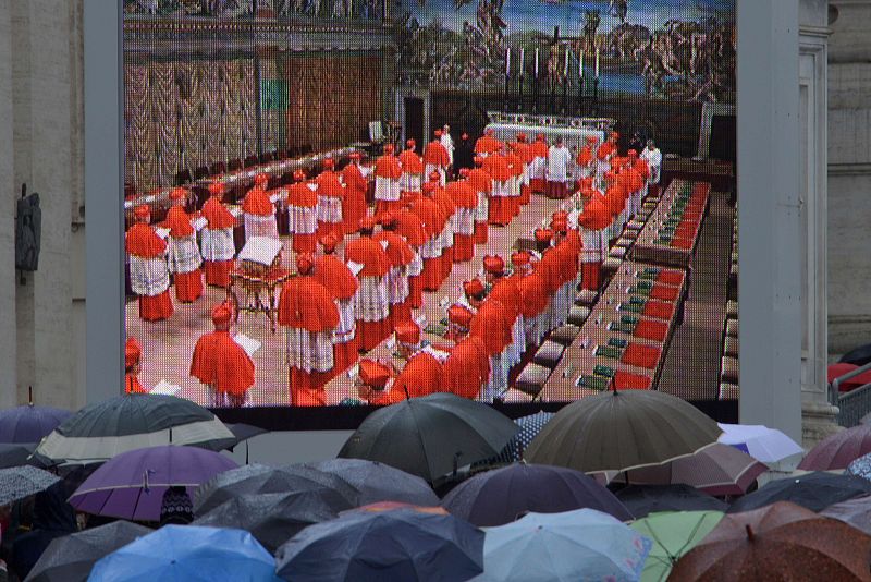 A pesar de la lluvia, una multitud observa la entrada de los cardenales en la Capilla Sixtina desde una pantalla gigante situada en la plaza de San Pedro