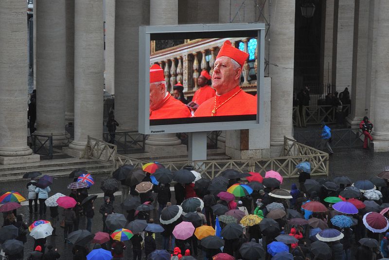 Una intensa lluvia cae sobre los presentes en la plaza de San Pedro del Vaticano mientras observan el inicio del cónclave en una pantalla gigante
