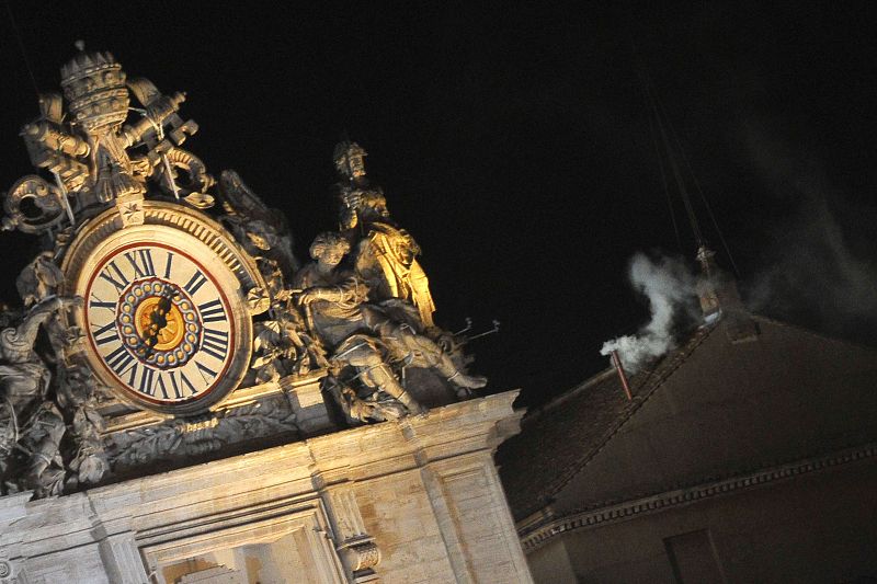 La chimenea deja salir el humo blanco tras el reloj de la basílica de San Pedro.