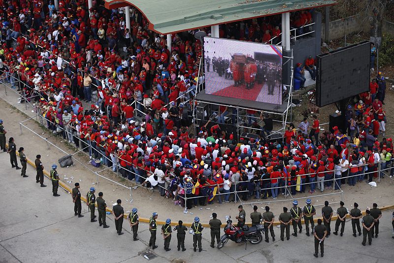 Algunos de los asistentes observan el traslado del féretro en una pantalla gigante instalada en las calles de Caracas