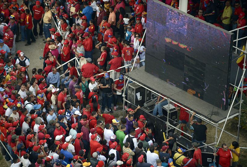 Decenas de personas observan en una pantalla instalada en las calles de Caracas el recorrido del coche fúnebre