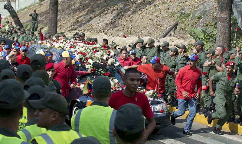 Algunos miembros de la "marea roja" depositan flores sobre el coche fúnebre que transporta el féretro de Chávez hasta el Cuartel del Monte