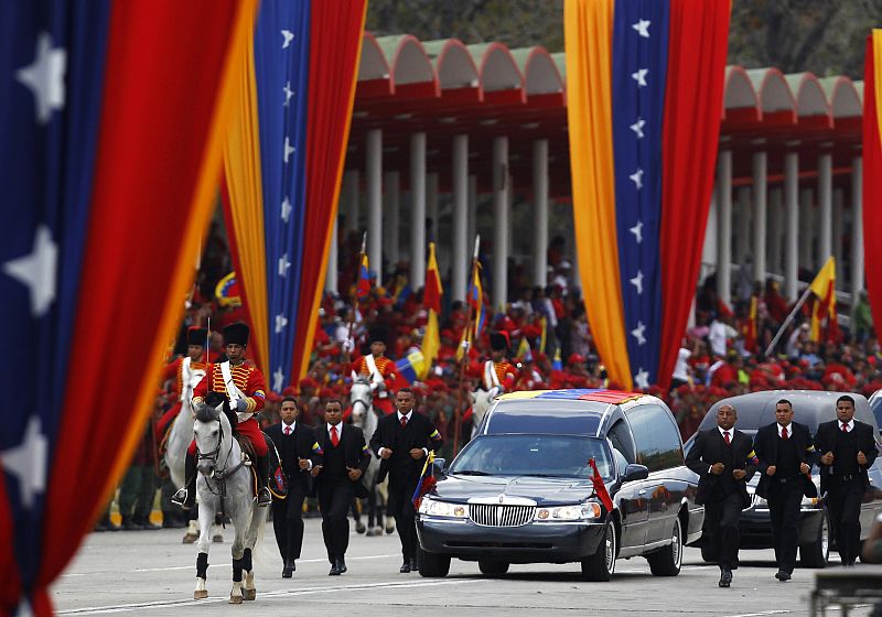 Guards run next to the hearse holding the body of Venezuela's late President Hugo Chavez during his funeral parade in Caracas