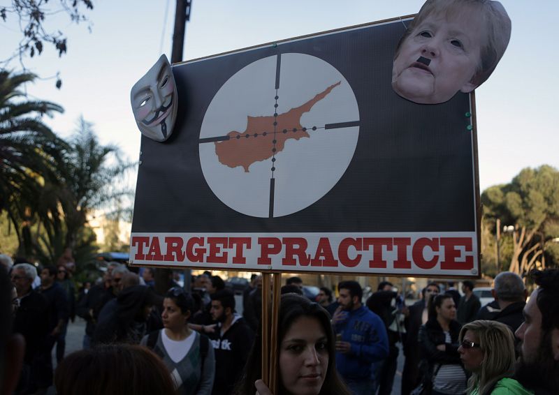 Una pancarta muestra las palabras "entrenamiento de tiro", con Chipre en el centro de la diana y una caricatura de Angela Merkel