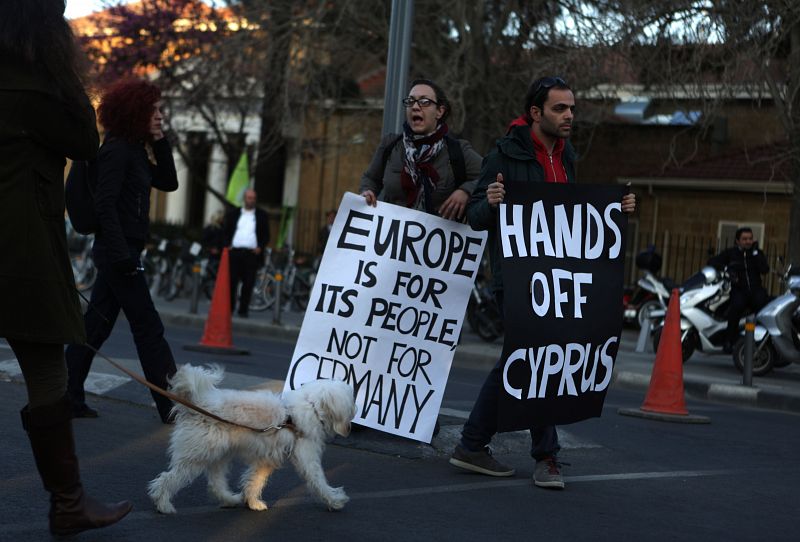 Dos jóvenes sostienen dos carteles con los lemas "Europa es para su gente, no para Alemania" (izquierda) y "Quitad las manos de Chipre" (derecha), en referencia al rescate financiero de Chipre.