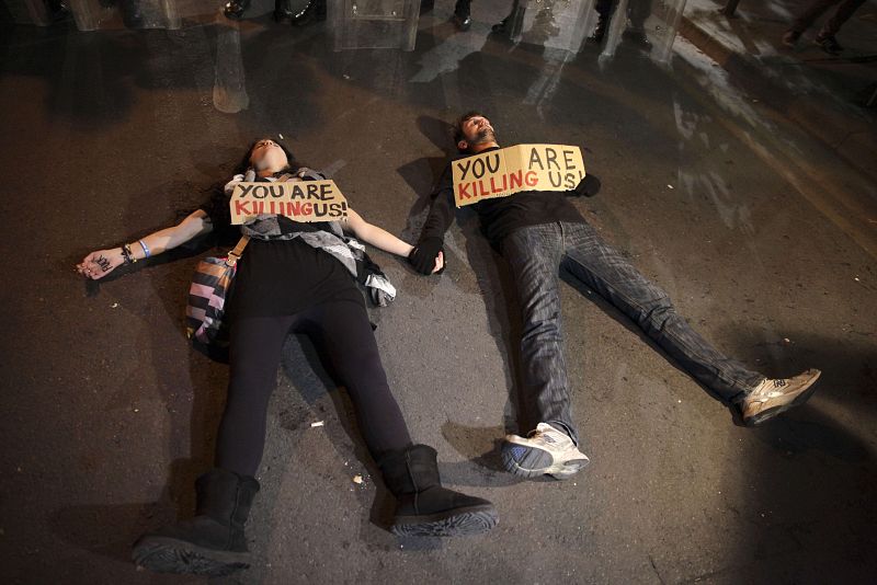 Dos manifestantes yacen en el asfalto con dos carteles en los que se lee, en inglés, "nos estáis matando", en referencia a las presiones económicas recibidas por Chipre