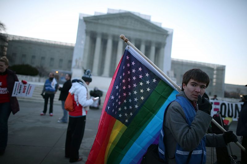 Un manifestante sostiene una bandera estadounidense que ha conservado las estrellas, pero cuyas barras han sido sustituidas por las franjas de la bandera arcoiris.