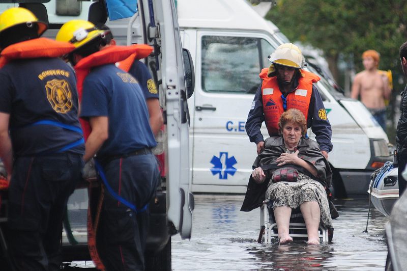 Los bomberos evacuan a una anciana en silla de ruedas por la inundación en La Plata, Argentina