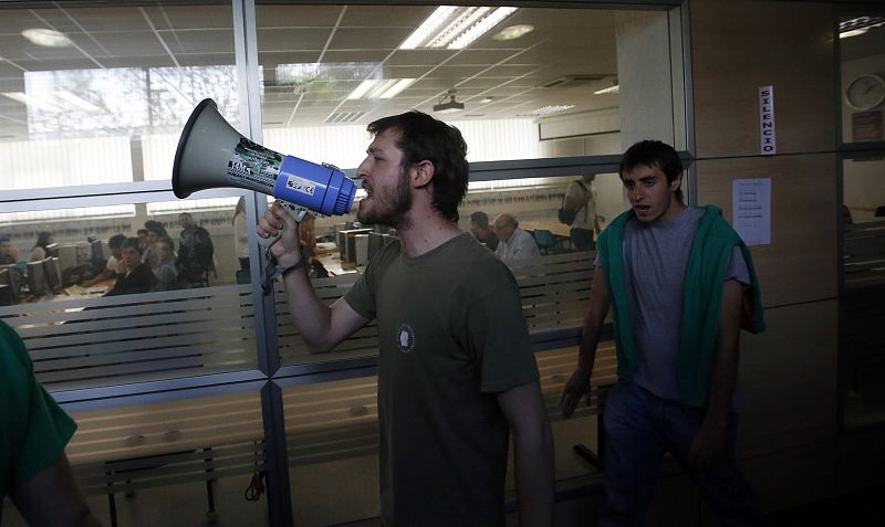 A picketer uses a megaphone to shout slogans as students look from a library inside the Telecoms Faculty at Madrid's Complutense University