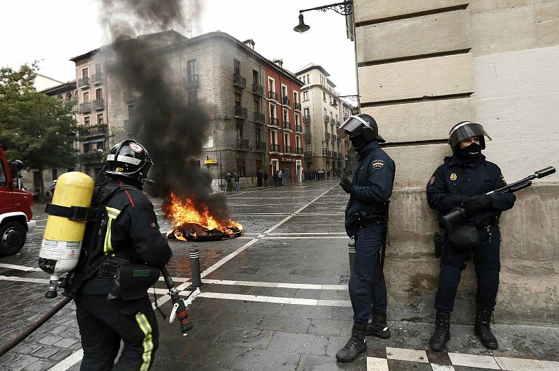 Un bombero se dispone a extinguir el fuego provocado por un grupo de jóvenes en un contenedor tras la manifestación de Pamplona