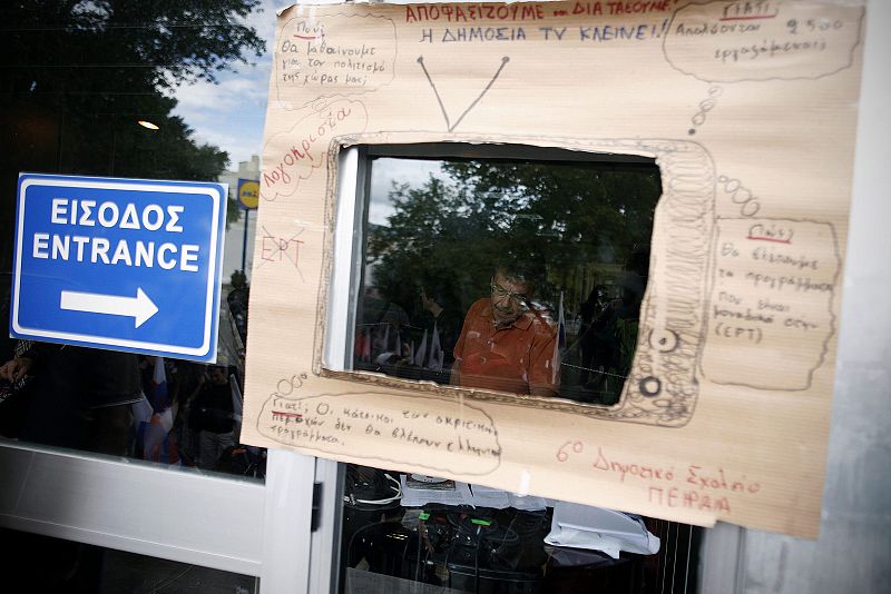 Vista de un cartel que muestra un dibujo de una televisión a través del que se observa a un periodista griego de la radiotelevisión pública del país ERT