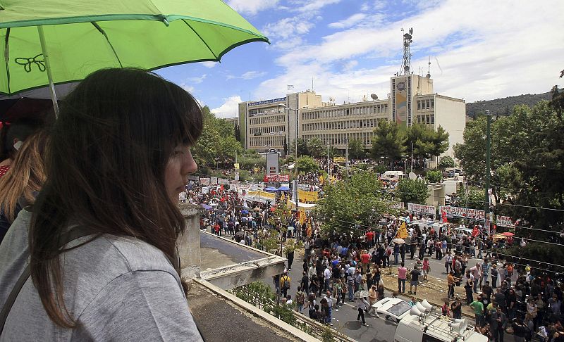 Una mujer observa a los manifestantes concentrados a las puertas de la sede central de la radiotelevisión pública griega