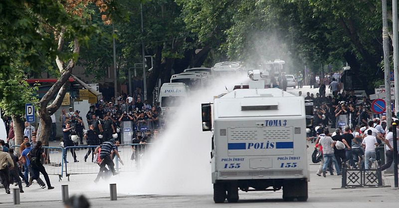 Camión policial y manifestantes huyendo de los chorros de agua lanzados por la Policía.