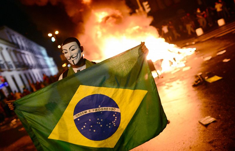 Un manifestante porta la bandera de Brasil frente a una de las hogueras que se han encendido en las calles de Rio de Janeiro