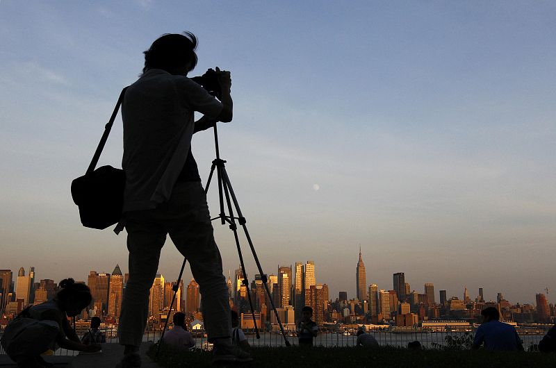 Una mujer fotografía la luna sobre el perfil de Nueva York