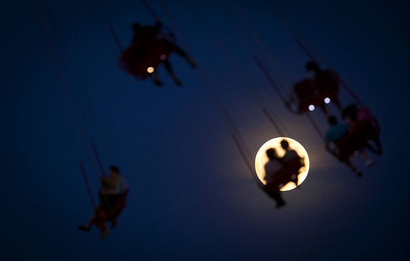 Los pasajeros de una atracción en Coney Island (Nueva York) se recortan contra la Superluna