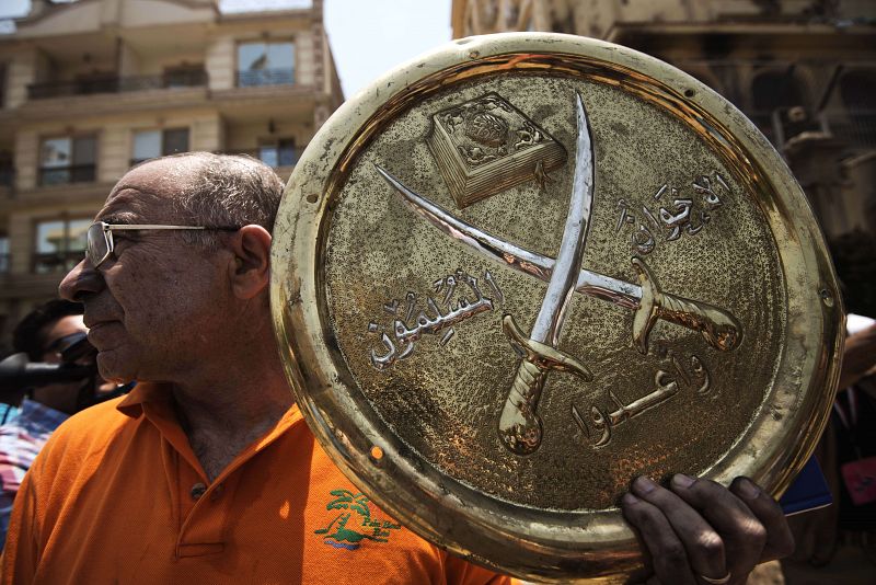 Un hombre sostiene uno de los emblemas de los Hermanos Musulmanes, arrancados por los asaltantes de la sede del grupo en El Cairo