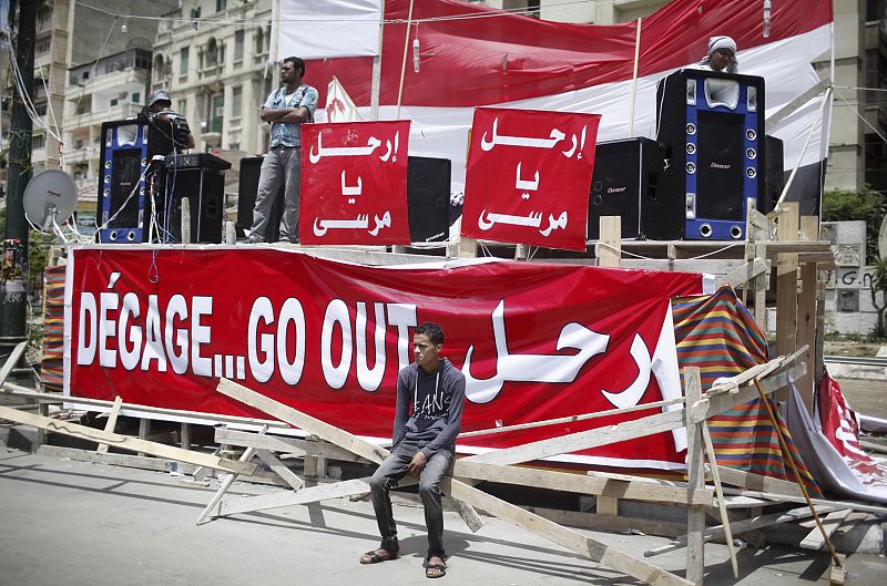 Un manifestante sentado en el escenario preparado en Alejandría. En el cartel puede leerse la invocación a que Morsi dimita.