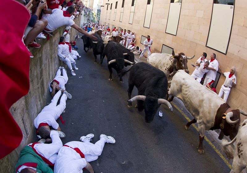 Unos corredores se tiran al suelo al paso de los toros de la ganadería de Valdefresno en la calle de Santo Domingo en el tercer encierro de San Fermín